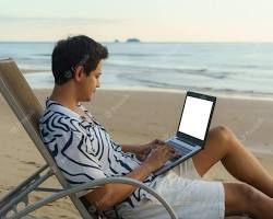 travel blogger working on their laptop while sitting on a beach